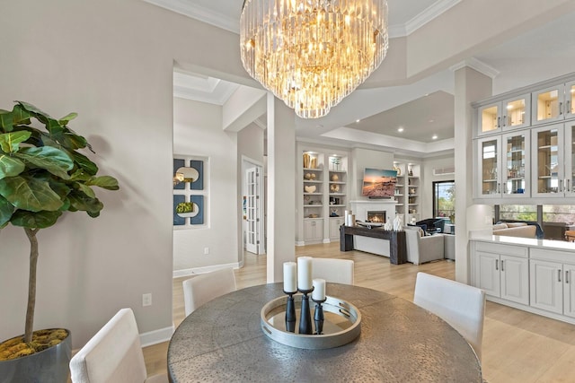 dining area with a tray ceiling, crown molding, light hardwood / wood-style floors, and built in shelves