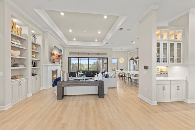 living room with built in features, light hardwood / wood-style flooring, ornamental molding, and a raised ceiling