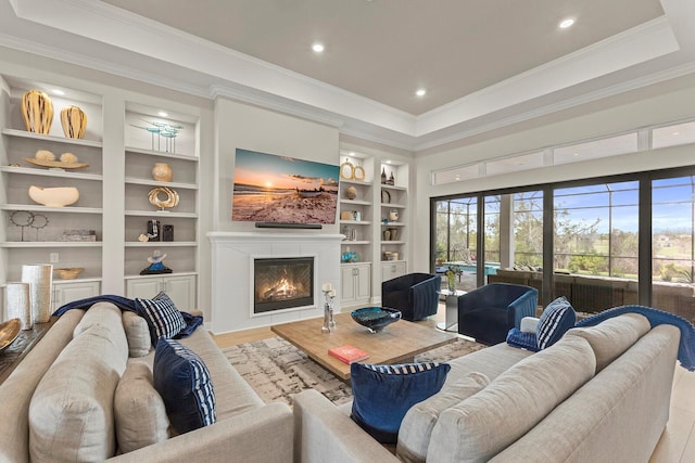 living room featuring a raised ceiling, ornamental molding, light wood-type flooring, and built in shelves