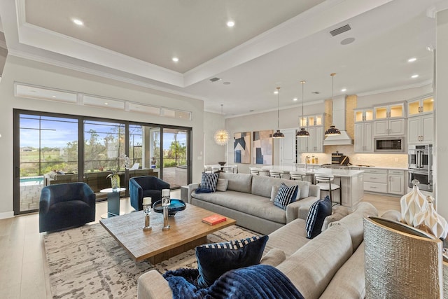 living room with crown molding, a tray ceiling, and light hardwood / wood-style flooring