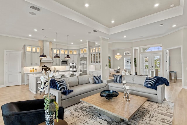 living room featuring sink, ornamental molding, a raised ceiling, french doors, and light wood-type flooring