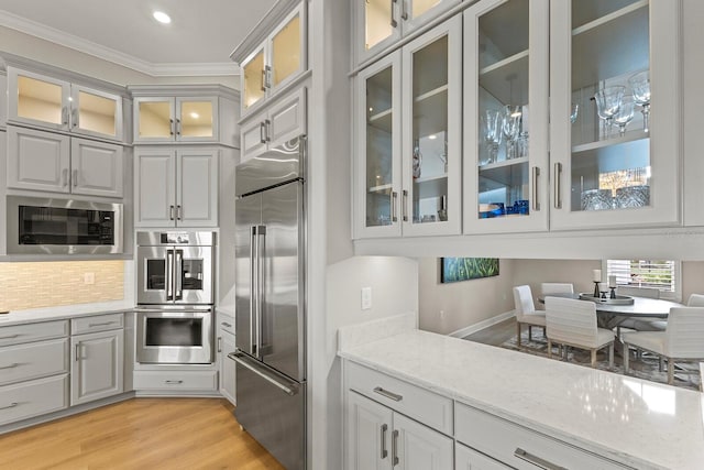 kitchen with crown molding, built in appliances, light stone countertops, light hardwood / wood-style floors, and backsplash