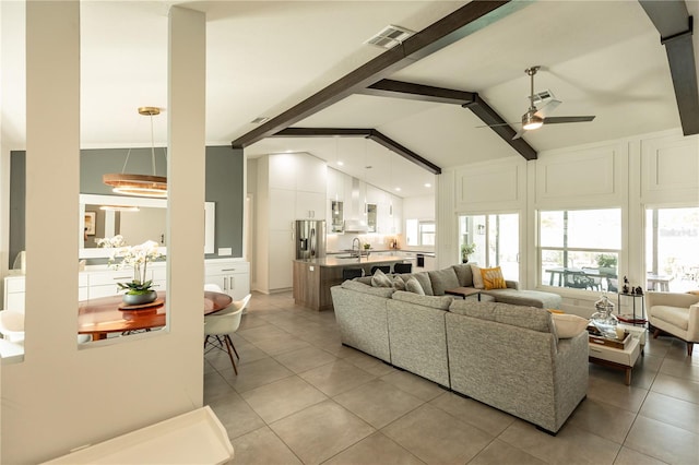 living area featuring ceiling fan, light tile patterned floors, visible vents, and beam ceiling