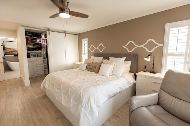 bedroom with a barn door, ensuite bath, ornamental molding, a walk in closet, and light wood-style floors