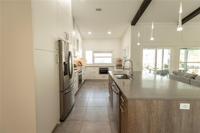 kitchen featuring light tile patterned flooring, stainless steel appliances, a sink, visible vents, and a center island with sink