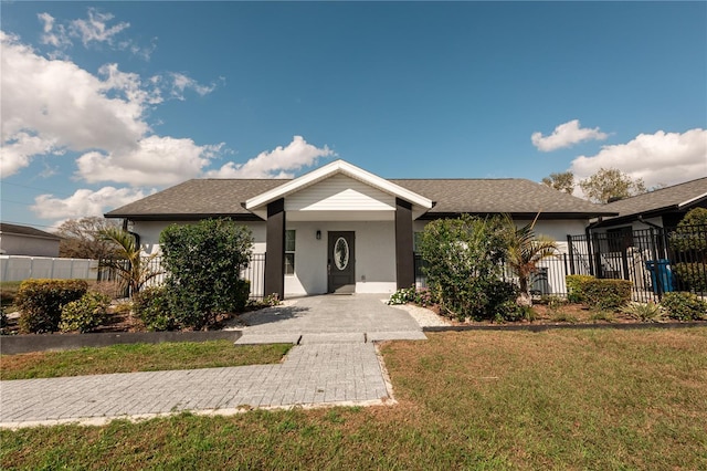 view of front of home featuring a shingled roof, fence, a front lawn, and stucco siding