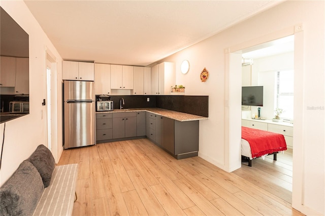 kitchen featuring freestanding refrigerator, gray cabinets, a sink, and light wood-style flooring