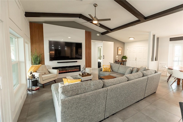 living room featuring lofted ceiling with beams, light tile patterned flooring, a wealth of natural light, and a glass covered fireplace