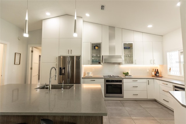 kitchen with lofted ceiling, a sink, white cabinetry, appliances with stainless steel finishes, and wall chimney exhaust hood