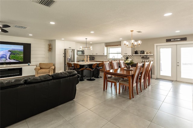 dining room with ceiling fan with notable chandelier, french doors, visible vents, and light tile patterned floors