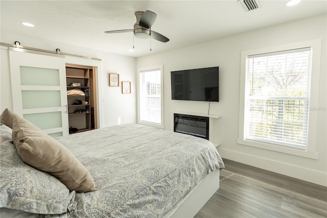 bedroom featuring wood finished floors, multiple windows, visible vents, and a barn door