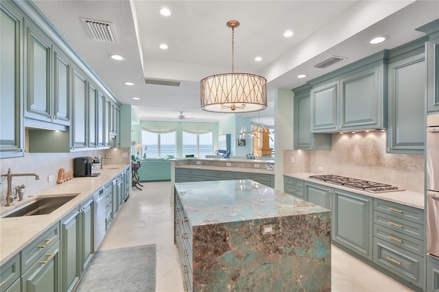 kitchen with a kitchen island, appliances with stainless steel finishes, pendant lighting, sink, and light stone counters