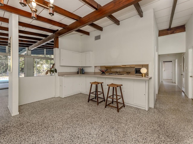 kitchen with a breakfast bar, beam ceiling, high vaulted ceiling, white cabinets, and kitchen peninsula