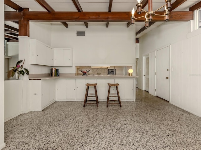 kitchen with a breakfast bar, an inviting chandelier, beam ceiling, white cabinets, and kitchen peninsula