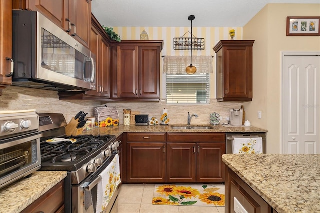 kitchen with appliances with stainless steel finishes, pendant lighting, tasteful backsplash, sink, and light stone counters