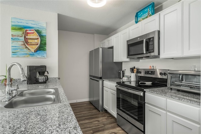 kitchen featuring appliances with stainless steel finishes, dark hardwood / wood-style floors, white cabinetry, sink, and light stone counters