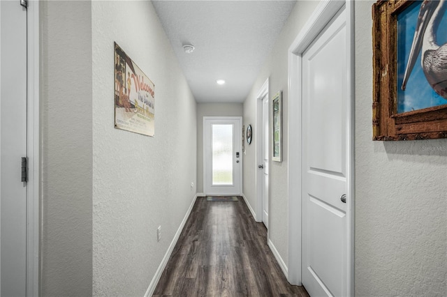hall with a textured wall, baseboards, and dark wood-style floors