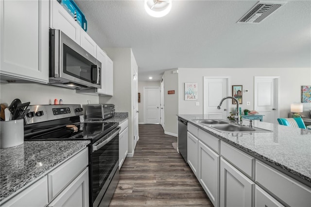 kitchen featuring a sink, stainless steel appliances, visible vents, stone counters, and dark wood-style floors