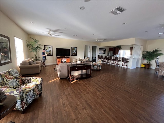 living room featuring wood finished floors, visible vents, baseboards, and ceiling fan