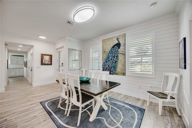 dining area featuring ornamental molding, light hardwood / wood-style floors, wood walls, and a textured ceiling