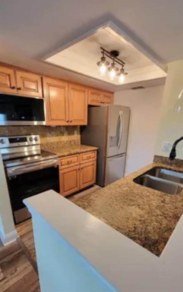 kitchen with a raised ceiling, appliances with stainless steel finishes, sink, and kitchen peninsula