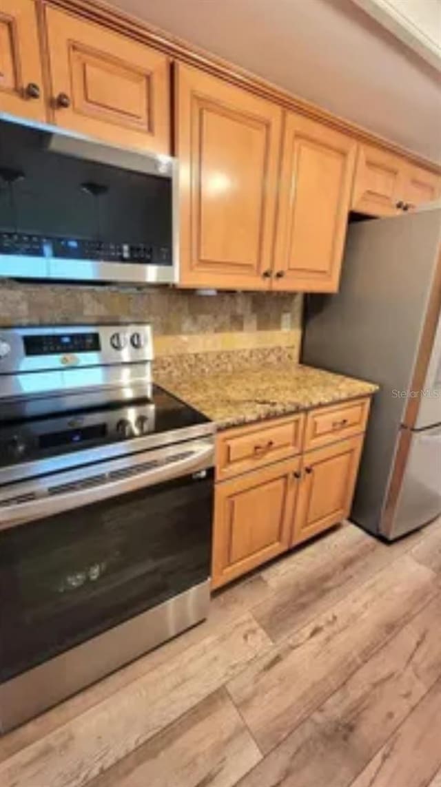 kitchen with light stone counters, appliances with stainless steel finishes, and light hardwood / wood-style flooring