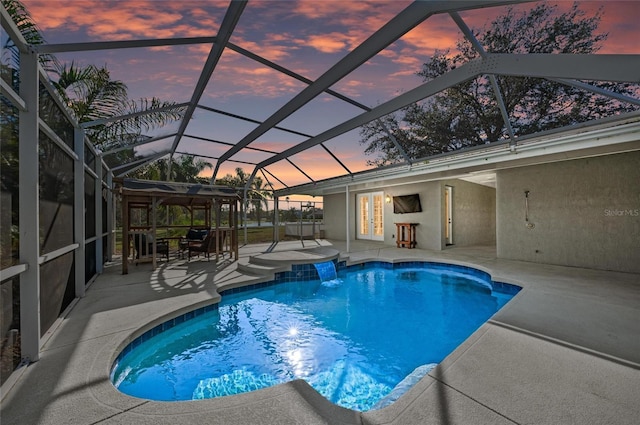 pool at dusk with pool water feature, a lanai, and a patio