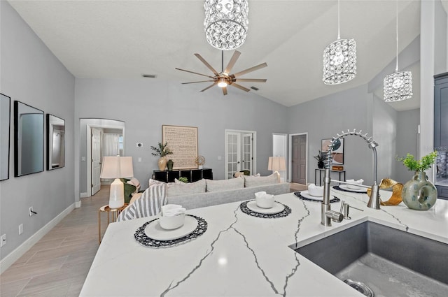 kitchen with hanging light fixtures, ceiling fan with notable chandelier, light stone counters, and french doors