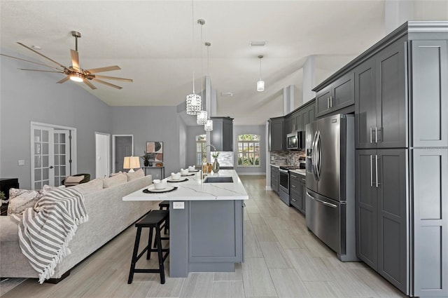 kitchen with gray cabinets, sink, hanging light fixtures, stainless steel appliances, and a center island with sink