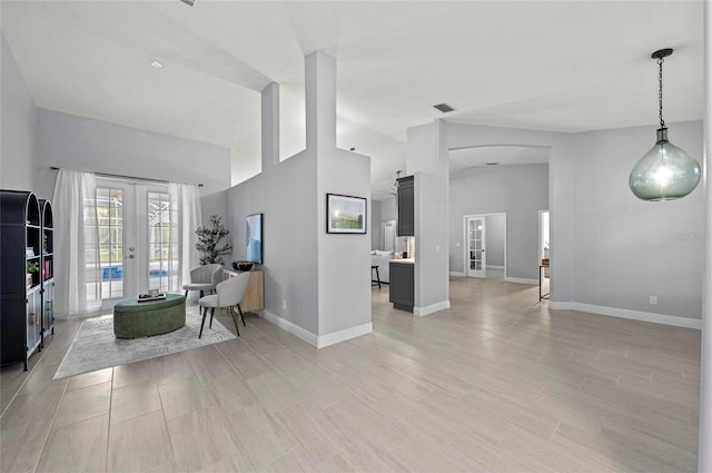 unfurnished living room with high vaulted ceiling, french doors, and light wood-type flooring