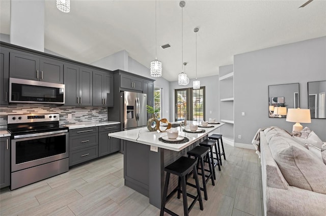 kitchen featuring a breakfast bar, decorative light fixtures, an island with sink, stainless steel appliances, and backsplash