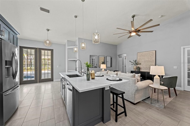 kitchen with decorative light fixtures, sink, a kitchen island with sink, stainless steel appliances, and french doors