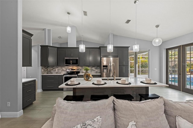 kitchen featuring tasteful backsplash, decorative light fixtures, stainless steel appliances, and an island with sink