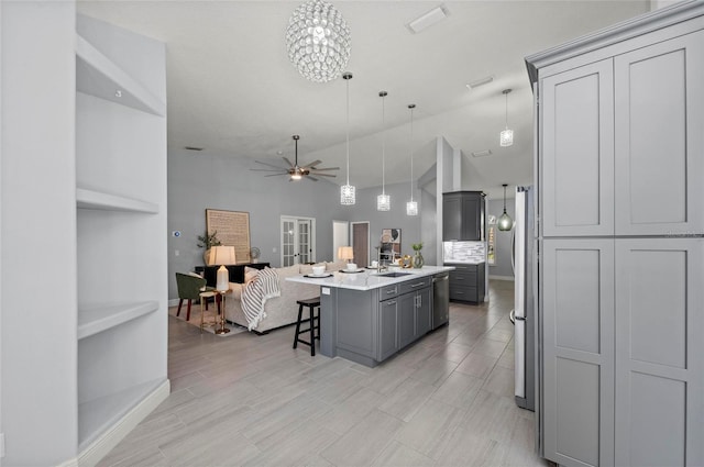 kitchen featuring sink, gray cabinetry, a kitchen breakfast bar, a center island with sink, and decorative light fixtures