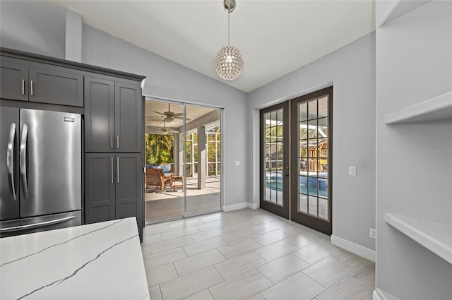 kitchen with lofted ceiling, stainless steel fridge, hanging light fixtures, light stone counters, and french doors