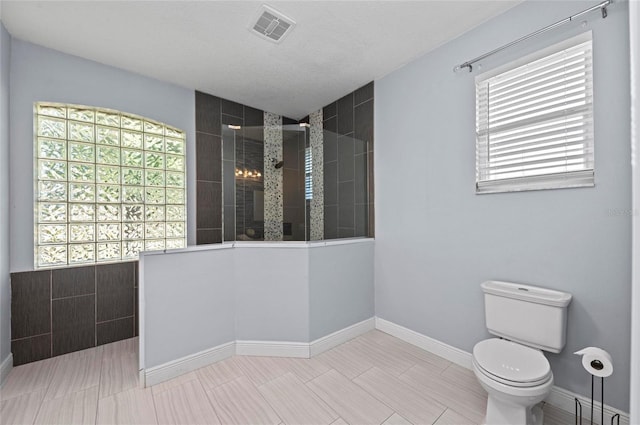 bathroom with a tile shower, a textured ceiling, and toilet