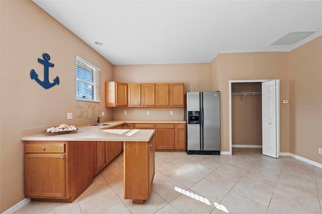 kitchen with light tile patterned flooring, stainless steel fridge, kitchen peninsula, and sink