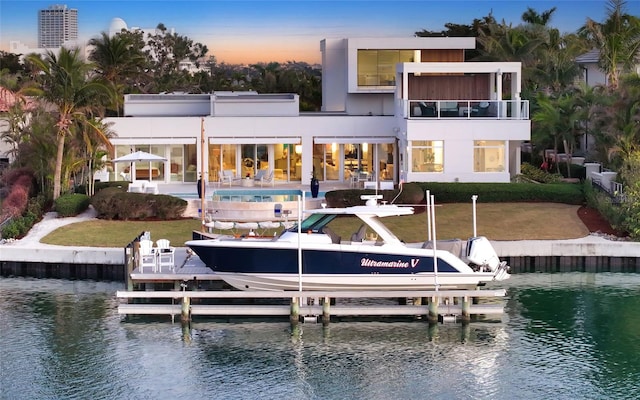 back house at dusk featuring a community pool, a yard, a patio, a water view, and a balcony