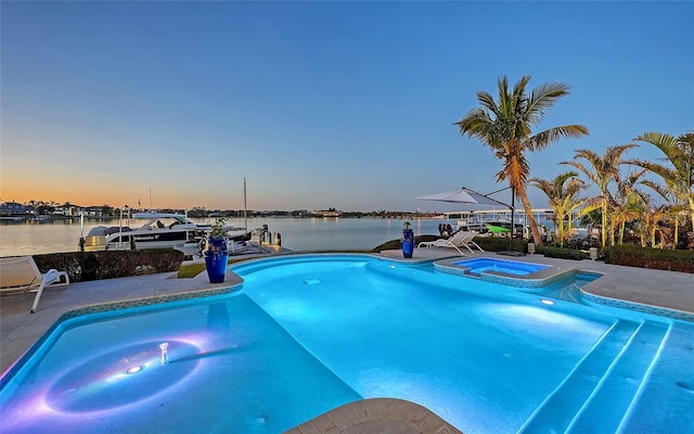 pool at dusk featuring a water view and an in ground hot tub