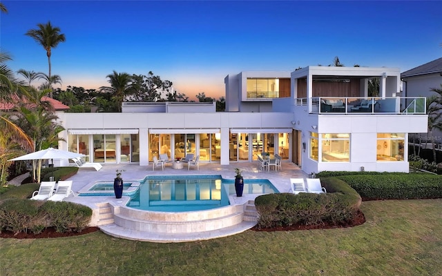 back house at dusk featuring a pool with hot tub, a yard, a patio area, and a balcony