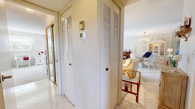 corridor with an inviting chandelier, light tile patterned floors, and a textured ceiling