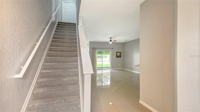 staircase with a ceiling fan, a textured wall, baseboards, and tile patterned floors