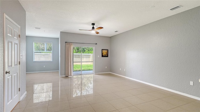 spare room with a textured ceiling, a textured wall, light tile patterned flooring, visible vents, and baseboards