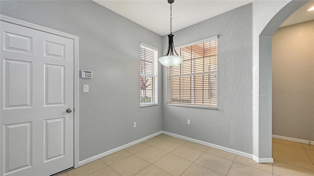 unfurnished dining area featuring light tile patterned floors, baseboards, arched walkways, and a textured wall