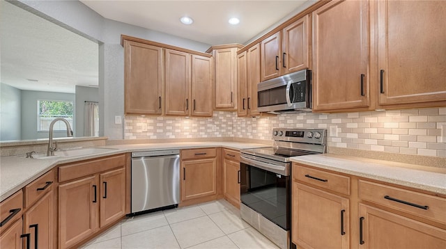 kitchen with light tile patterned floors, a sink, light countertops, appliances with stainless steel finishes, and backsplash