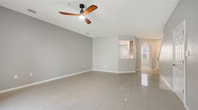 unfurnished room featuring visible vents, arched walkways, baseboards, ceiling fan, and light tile patterned flooring