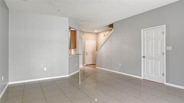 empty room with arched walkways, a textured wall, stairway, tile patterned flooring, and baseboards