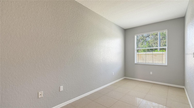 empty room with a textured ceiling, a textured wall, light tile patterned floors, and baseboards