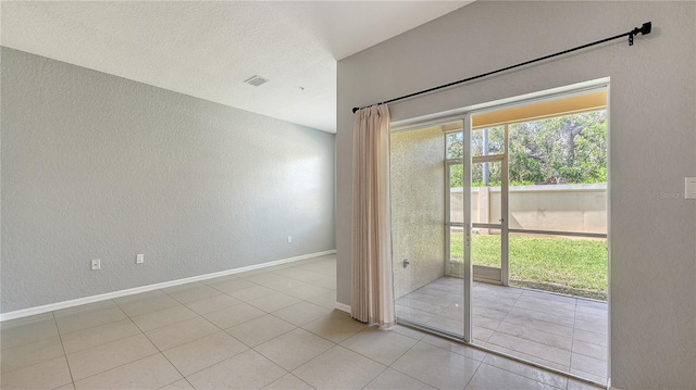 tiled spare room featuring visible vents, baseboards, a textured ceiling, and a textured wall