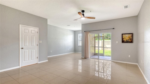 spare room with light tile patterned floors, a ceiling fan, and a textured wall